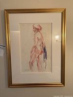 Framed watercolor figure study on wall with gold frame and white mat, showing a standing nude female figure in profile, signed bottom left.