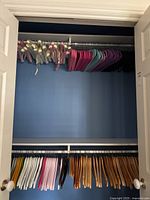 Closet showing multiple satin padded hangers in pink, cream, pale yellow, purple, and off-white colors along with foam hangers in pink and purple shades hung on upper rod, and wooden hangers below.