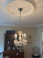 Large 5-light crystal chandelier hanging from ceiling, showing five candelabra bulbs and glass prisms.