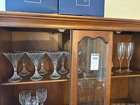 Mikasa crystal stemware displayed in wooden cabinet, includes martini glasses, champagne flutes, and salt shaker