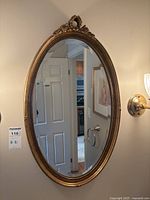 Full frontal view of the oval mirror mounted on a wall, showing its shape and gold ornate frame.