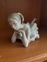 Front left angle shot of NAO ballerina figurine lying on stomach with detailed facial features and white ruffled tutu.