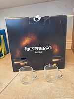 Nespresso Inissia box with two clear glass cups placed in front.