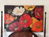Full view of the unframed floral painting showing red, orange, yellow, and white poppies on a dark background above a wooden furniture piece.