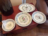 Four plates displayed on a wooden surface, showing floral and butterfly patterns on each.
