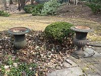 Two cast metal urns outdoors on stone pavers and leaves