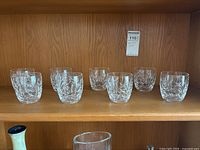 Eight Waterford crystal glasses arranged on a wooden shelf.