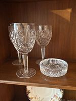 Three Waterford crystal wine glasses and one crystal ashtray displayed on a wooden shelf.
