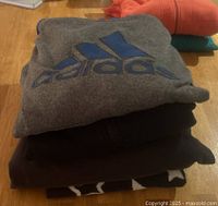 Stack of folded clothes with a visible grey Adidas sweatshirt with blue logo on top.