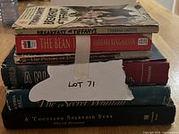 Stack of seven fiction books arranged on a table with a paper label LOT 71