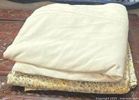Folded plain cream/off-white flat sheet on top of folded floral patterned flat sheet with yellow, grey, and cream flowers.