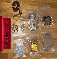 Full view of various jewelry pieces grouped together in plastic bags and a red jewelry box, plus rolled leather belt.