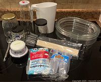 Clear glass jars, a white milk jug, Starfrit dicer, packs of disposable cups, bamboo skewers, and spoons on kitchen counter.