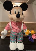 Full front view of the Mickey Mouse plush standing on a kitchen counter, showing outfit and flowers.