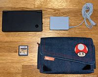 Top view of Nintendo DSi, charger, game cartridge, and carrying case arranged on wood surface