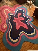 Full view of rug showing irregular abstract contour design in pink, blue, navy and white on hardwood floor.