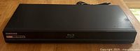 Front and top view of black Samsung Blu-ray Disc/DVD player showing logos and overall condition.