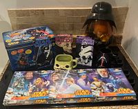 Star Wars collectible items including Mr. Potato Head tin, three VHS tapes, three mugs including Yoda and Darth Vader themes, and three unopened puzzles.