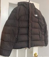 Full view of black puffer jacket showing the design, hood, and The North Face logo on chest.