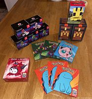 Wide view of assorted unopened toys and card sets including Nintendo Mario Kart figures, Pokémon cards, McDonald's pixel collectibles, and a Yu-Gi-Oh figure on a wooden table.