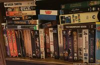 Shelf of assorted VHS movies showing titles like Nevada Smith, The Magnificent Seven, E.T., and others.