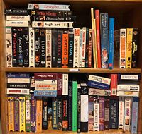 Shelf showing 28 VHS tapes and several books packed closely together.