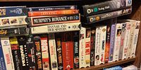 Wide view of VHS and DVD collection on shelves showing movie titles and cases.