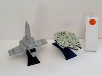 Side view showing gray Imperial Shuttle and white Millennium Falcon on stands, with a white box with a #14 orange sticker in the background.