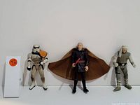 Photo showing three collectible Star Wars action figures against a white background: Clone Trooper, a cape-wearing figure with red lightsaber, and a gray pilot figure.