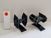 Two collectible Star Wars TIE Fighter figurines displayed on their black stands with the Star Wars logo, shown on a plain surface with a white tag marked with an orange circle and the number 8.