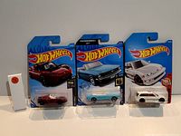 Three Hot Wheels collectible cars in blister packs: maroon sports car, blue Thunderball muscle car, white rally car.