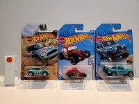 Photo showing three new Hot Wheels collectible cars in original packaging: a blue rally car, a red and black Volkswagen dune buggy, and a light blue and black off-road truck.