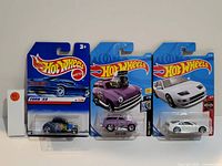 Photo of three new Hot Wheels cars in original packaging showing a blue Ford '32, a purple custom car with large engine, and a white Nissan 300ZX.