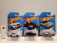 Photo of three new Hot Wheels collectible cars in original packaging, showing white BMW M2, black sports car, and silver Honda Prelude.