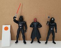 Photo showing three Star Wars figures: Darth Vader, Darth Maul, and Shadow Guard standing side by side against a light brown background.
