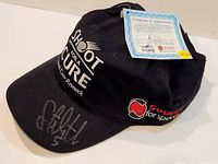 Black baseball cap signed with silver marker on the brim featuring 'Shot for a Cure' cancer research logo and 'Source for Sports' logo.