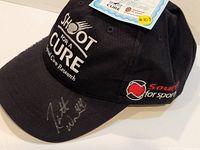 Front and side view showing 'Shoot for a Cure' text, 'Sound for Sports' logo, and autograph on brim.