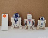 Three Star Wars droid collectibles including two R2-D2 figures and one different astromech droid figure.