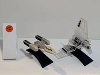 Photo showing two Star Wars starfighter figures: a Y-Wing and a TIE Interceptor on black display stands, with a small orange sticker numbered 45.