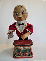 Front view of the vintage toy bartender figure in red jacket holding a shaker behind a bar counter.