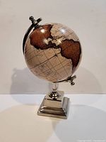 Side angle view of vintage desktop globe with brown continents and silver metal stand.