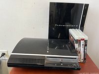 Two PlayStation 3 consoles side by side with 4 game cases stacked next to them.
