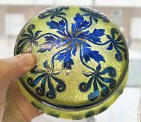 Top and side views of circular jewelry box showing intricate blue floral cameo etching on yellow-green crackled glass