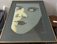 Close-up photo of the framed pastel painting showing the woman's face and artist's signature at bottom right dated 2002.