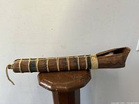Side view of tall wooden indigenous dart quiver holder lying on a stand, showing fiber bindings and carved details