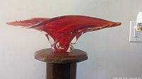 Front angle of the scarlet red abstract glass vase showing the winged shape and clear base.