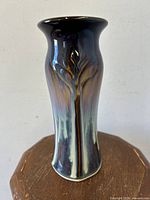 Front view of drip-glaze lotus flower pottery vase with dark blue and brown glaze, sign of artist Bill Campbell, standing on wooden surface.
