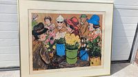 Framed lithograph showing group of people around a table with colorful flowers in pots, people wearing hats in various colors.