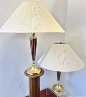 Both vintage mid-century modern table lamps side by side showing wood and brass bases with cream fabric pleated shades on and off.