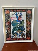 Front view of the framed abstract Judaica art print by Kopel Gurwin. Colorful artwork of two stylized figures with floral designs and Hebrew text framed in a white frame.